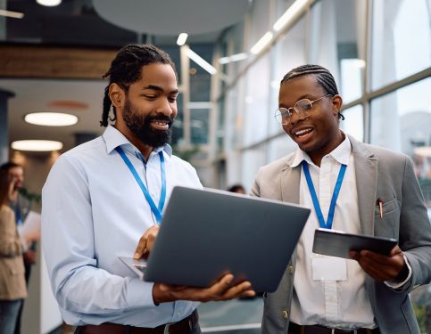African American businessmen using wireless technology in hallway of an office building.